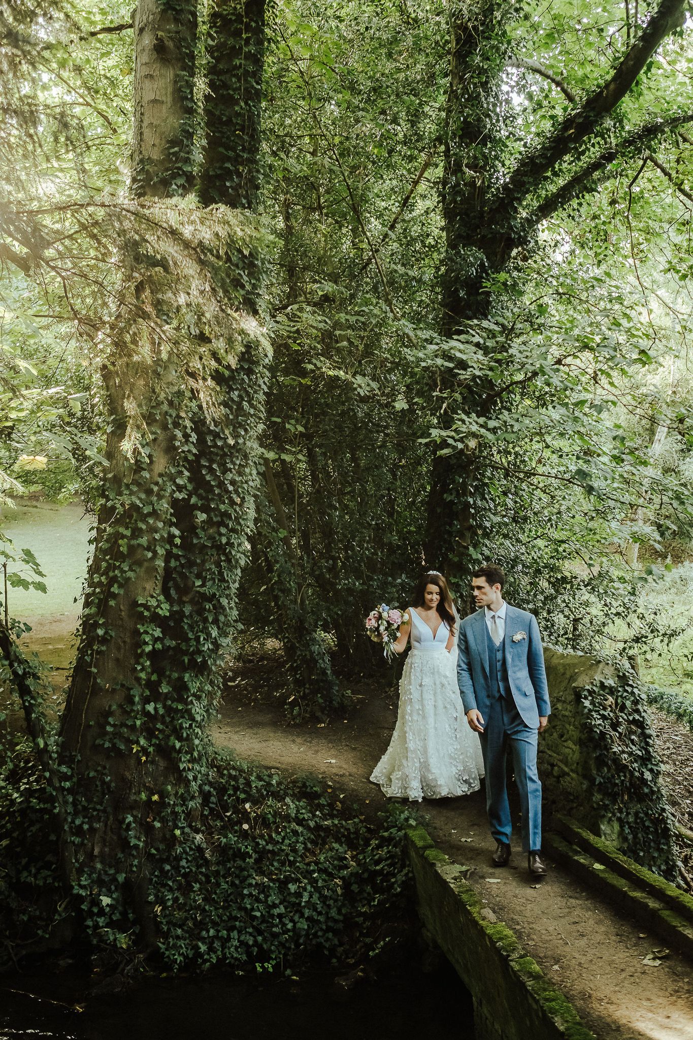 Couple walks along a moss-covered path surrounded by lush green forest.