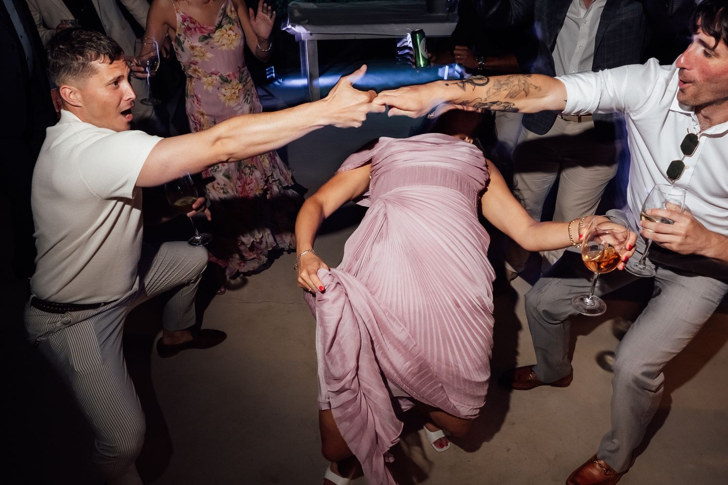 Guests dancing energetically at a wedding reception, woman in pink dress dipping on the dance floor.