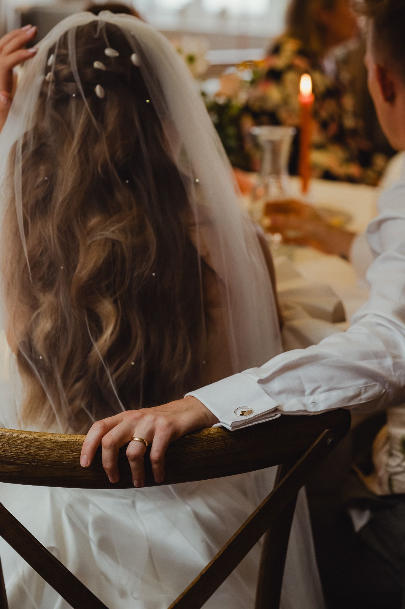 Close-up view of a bride's long wavy hair and white wedding dress detail at a candlelit reception.