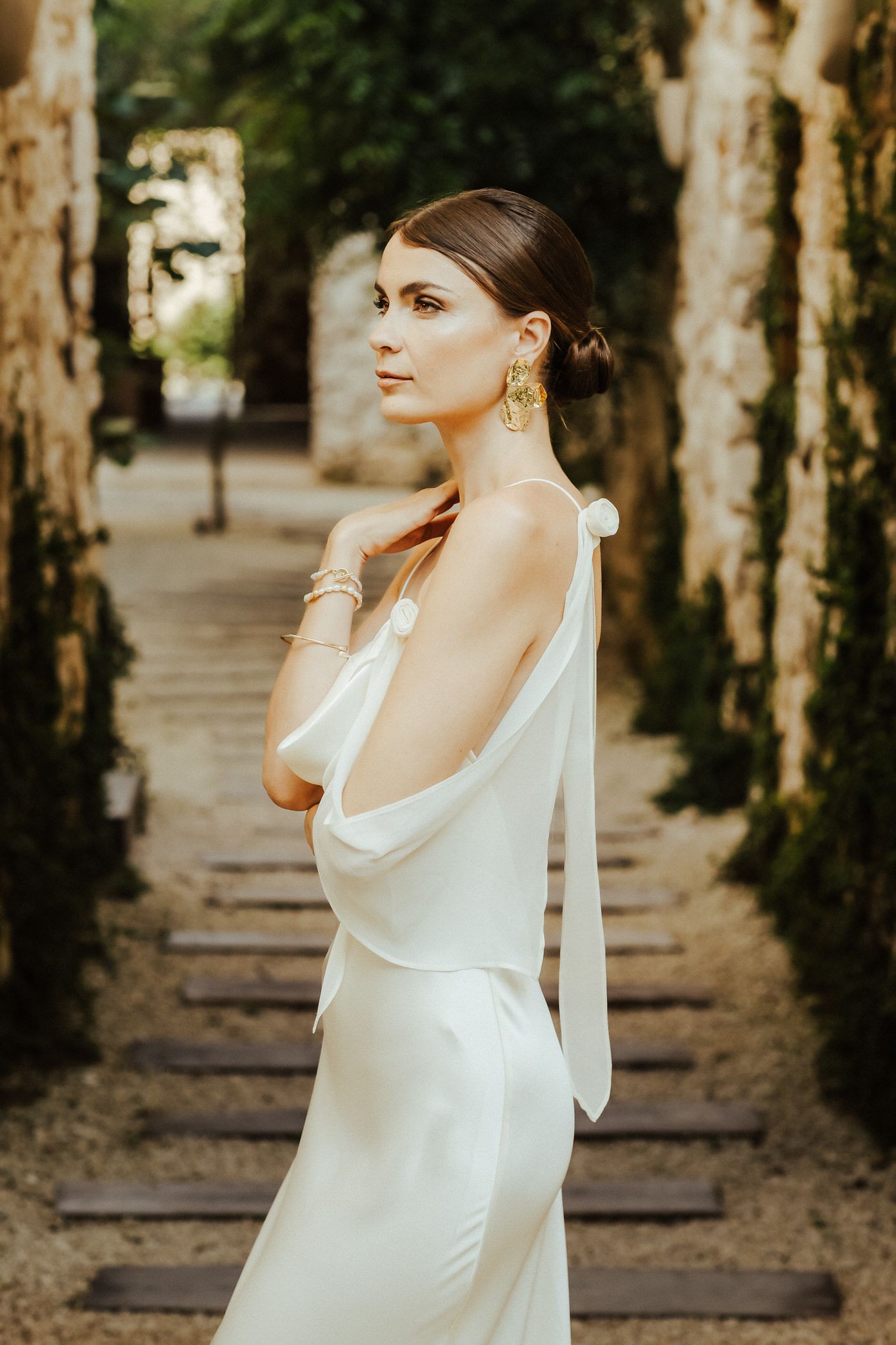 Elegant white flowing dress photographed in a tree-lined path with natural sunlight filtering through the branches.