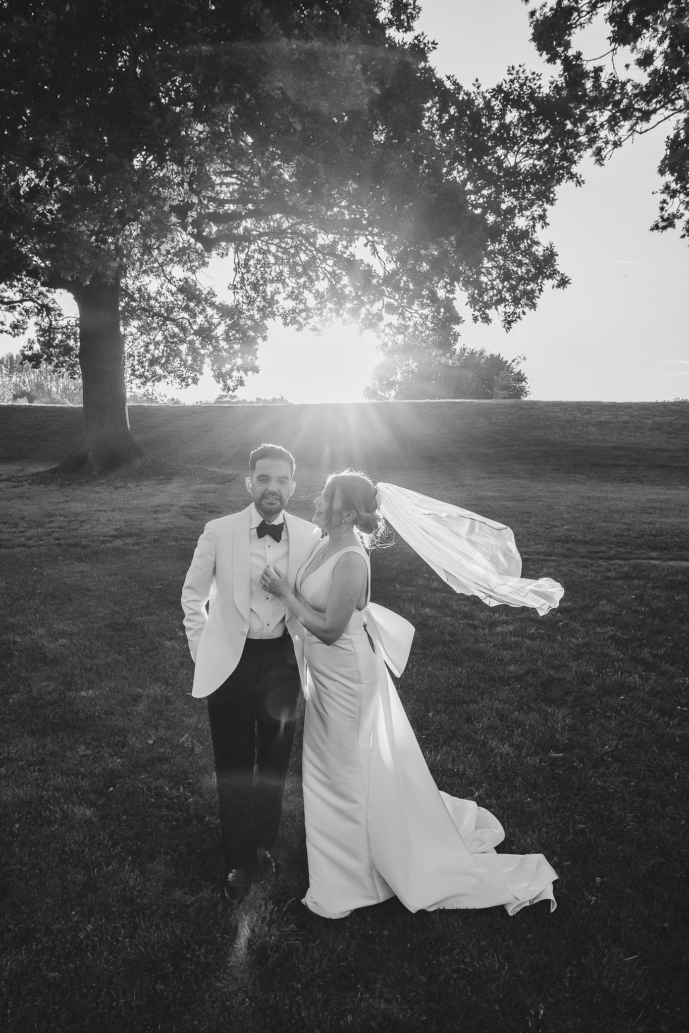 A romantic black and white wedding photo shows a couple dancing in a sunlit meadow as a veil flows in the breeze.