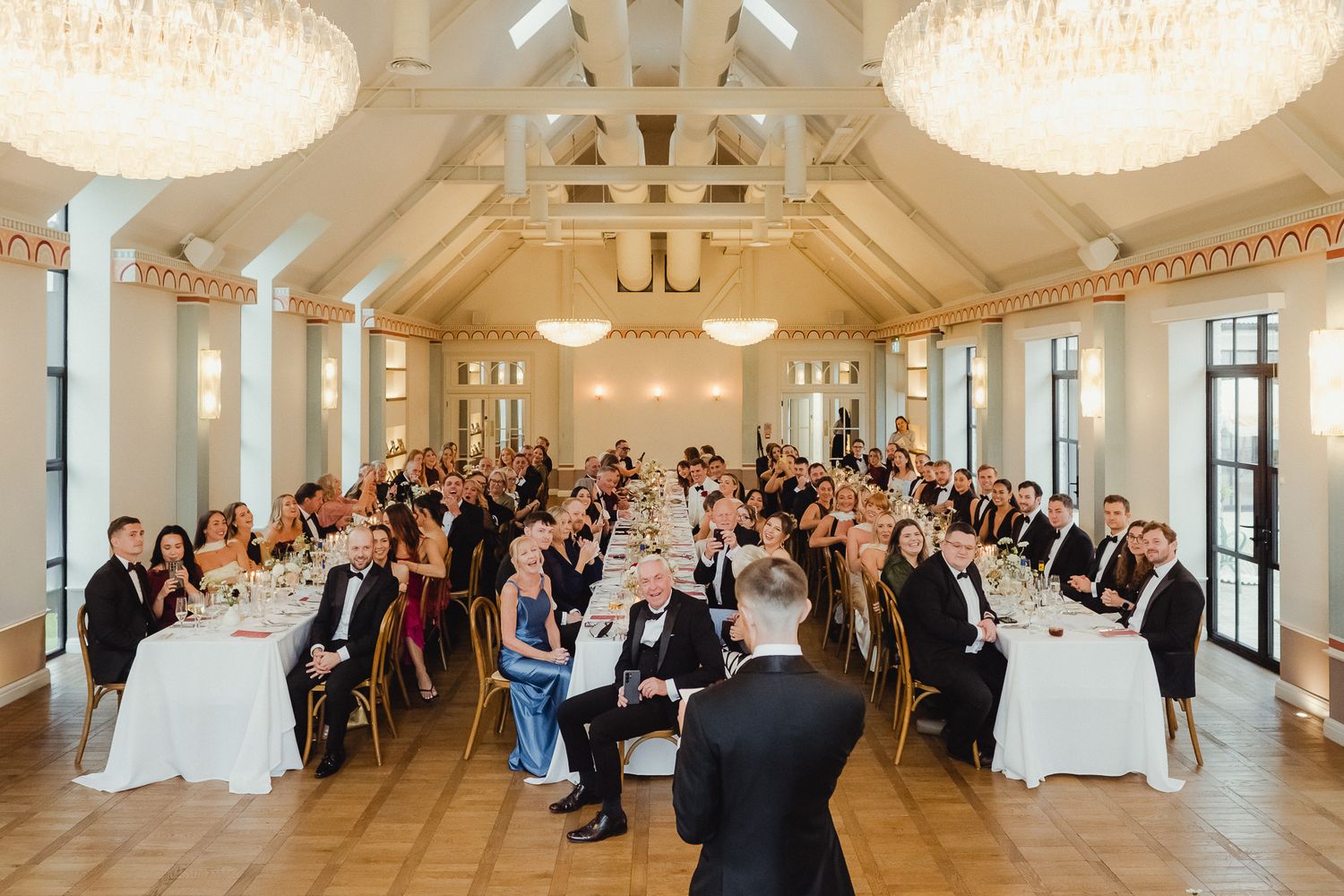 Panoramic view of an elegant white wedding ceremony venue with guests seated in rows beneath crystal chandeliers.