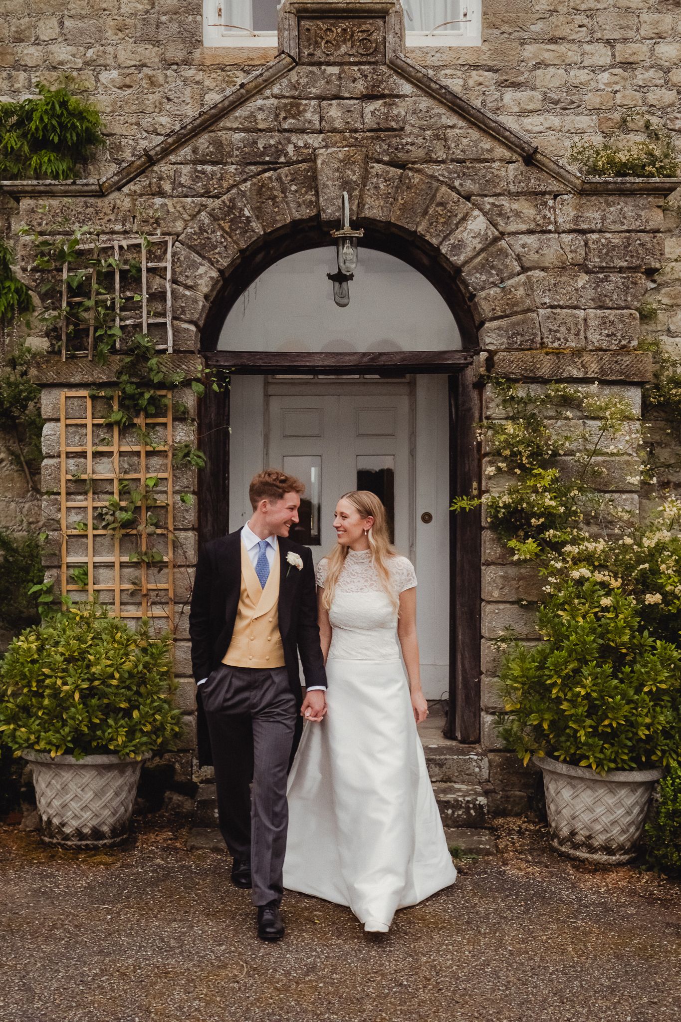 Romantic wedding couple posing together in front of a rustic stone wall entrance with arched doorway and garden trellis.