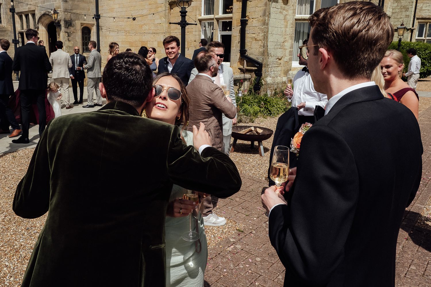 Guests socializing outdoors at a wedding reception, holding champagne glasses in a sunny courtyard setting.