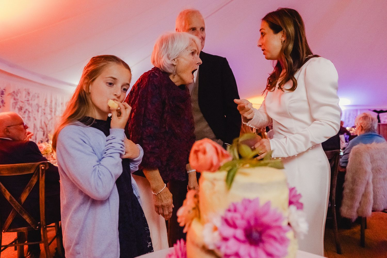 People dancing together at an event with pink and purple lighting and floral decorations.