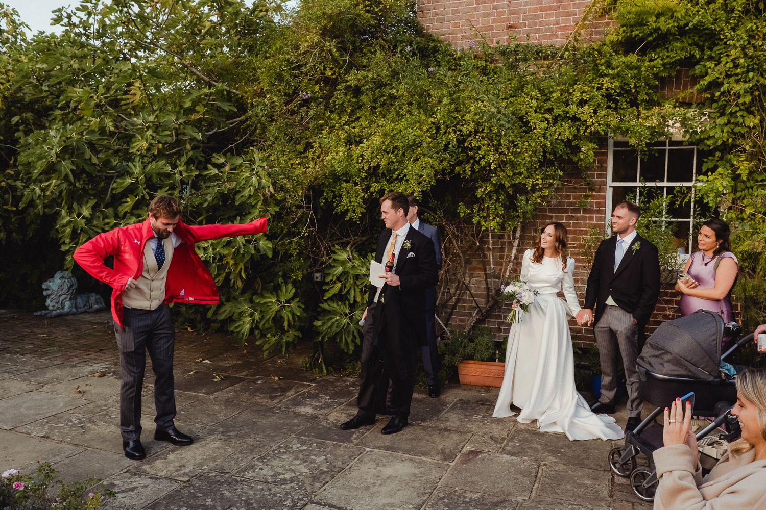 Wedding party gathers in a lush garden courtyard with brick walls and natural greenery for outdoor photos.