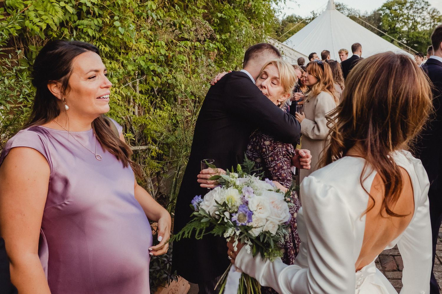 Guests celebrate and embrace during an outdoor wedding ceremony surrounded by lush greenery.