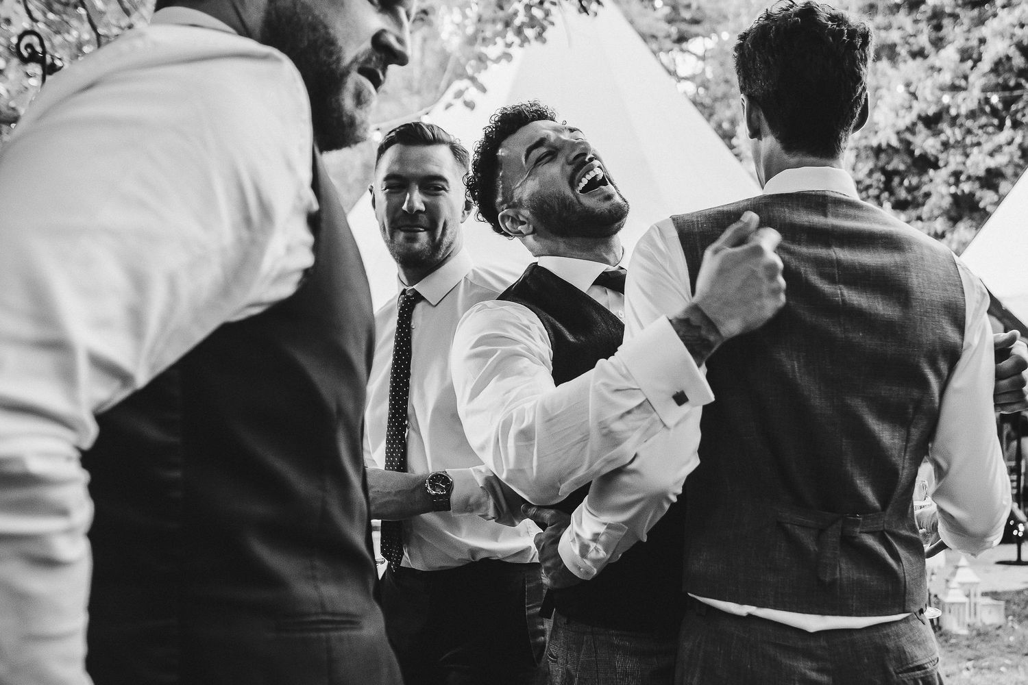 Groomsmen laugh together during candid wedding reception moment.