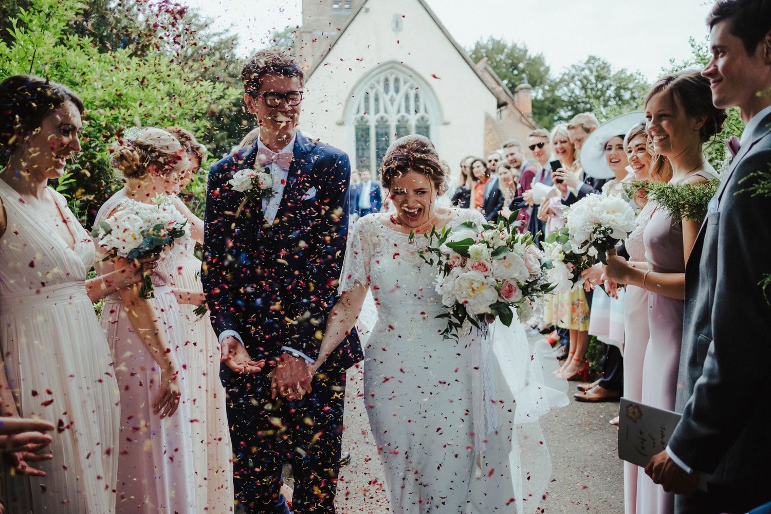 Joyful wedding celebration with confetti shower outside a stone church.