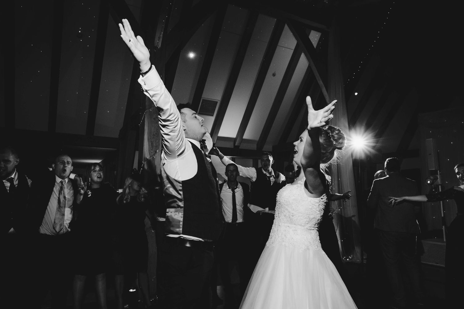 Wedding celebration with energetic dancing in a darkened reception venue.