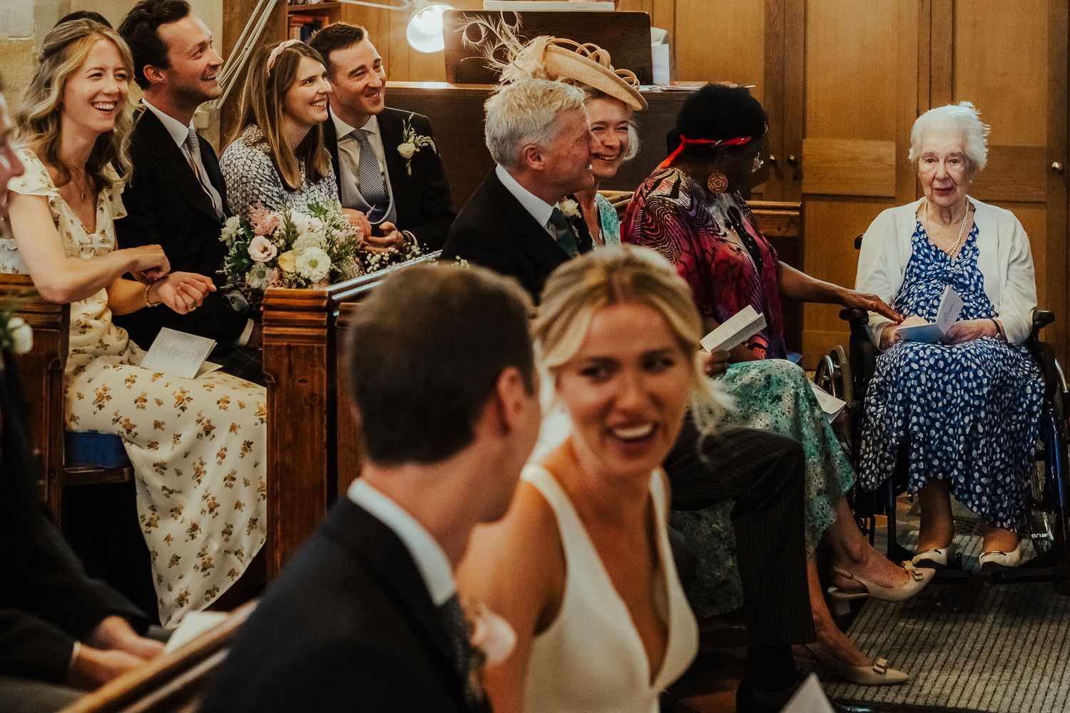 Wedding guests share joyful laughter during the ceremony in wooden church pews.