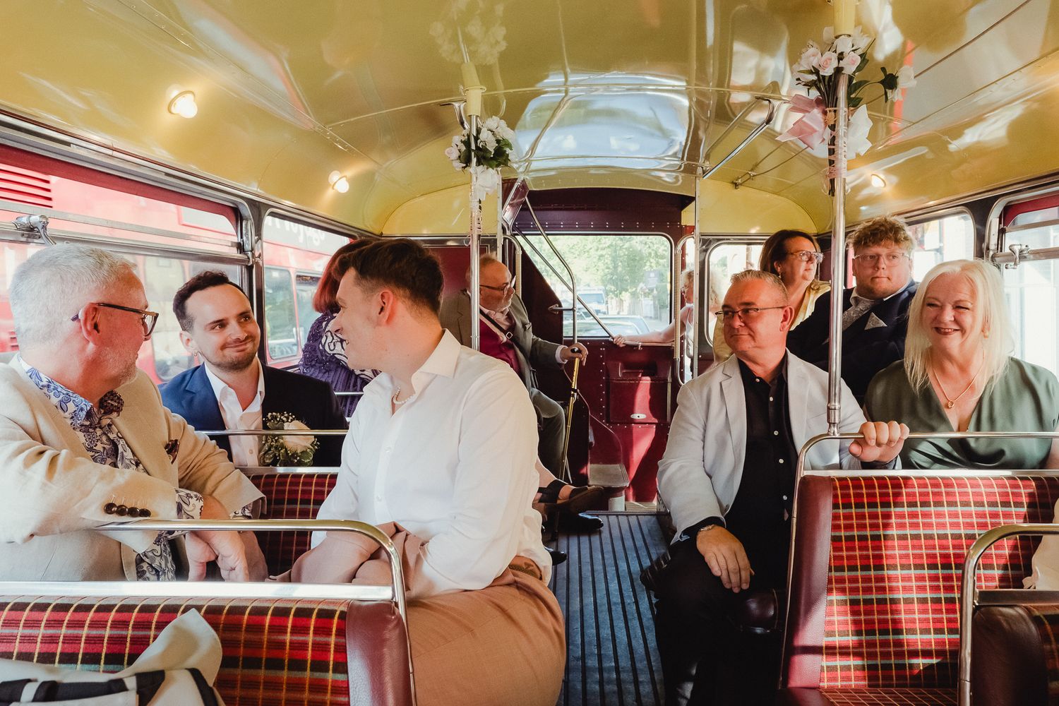 Passengers enjoy a social gathering and conversation while riding together on a vintage red double decker bus.