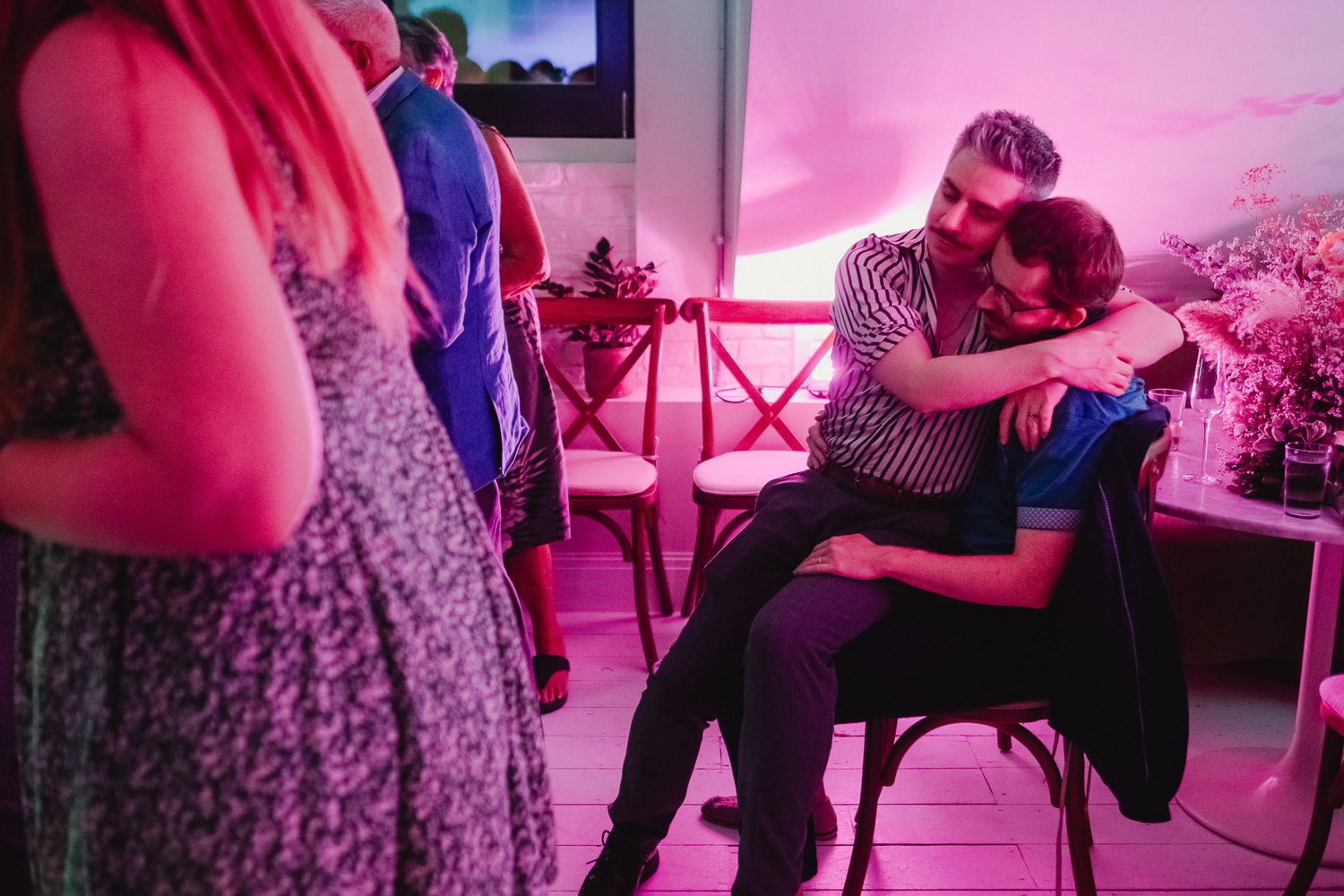 People dancing together in a dimly lit room with pink lighting and a festive atmosphere.