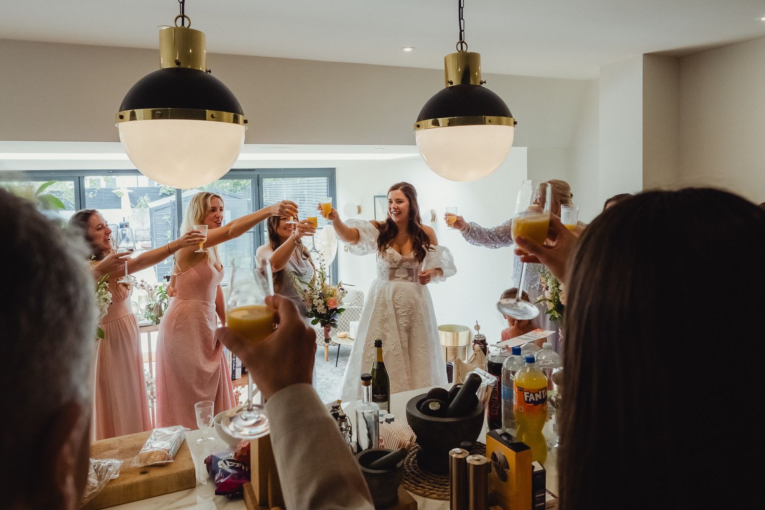 A celebratory moment at a gathering with people dancing and raising their hands under pendant lights in a bright interior space.