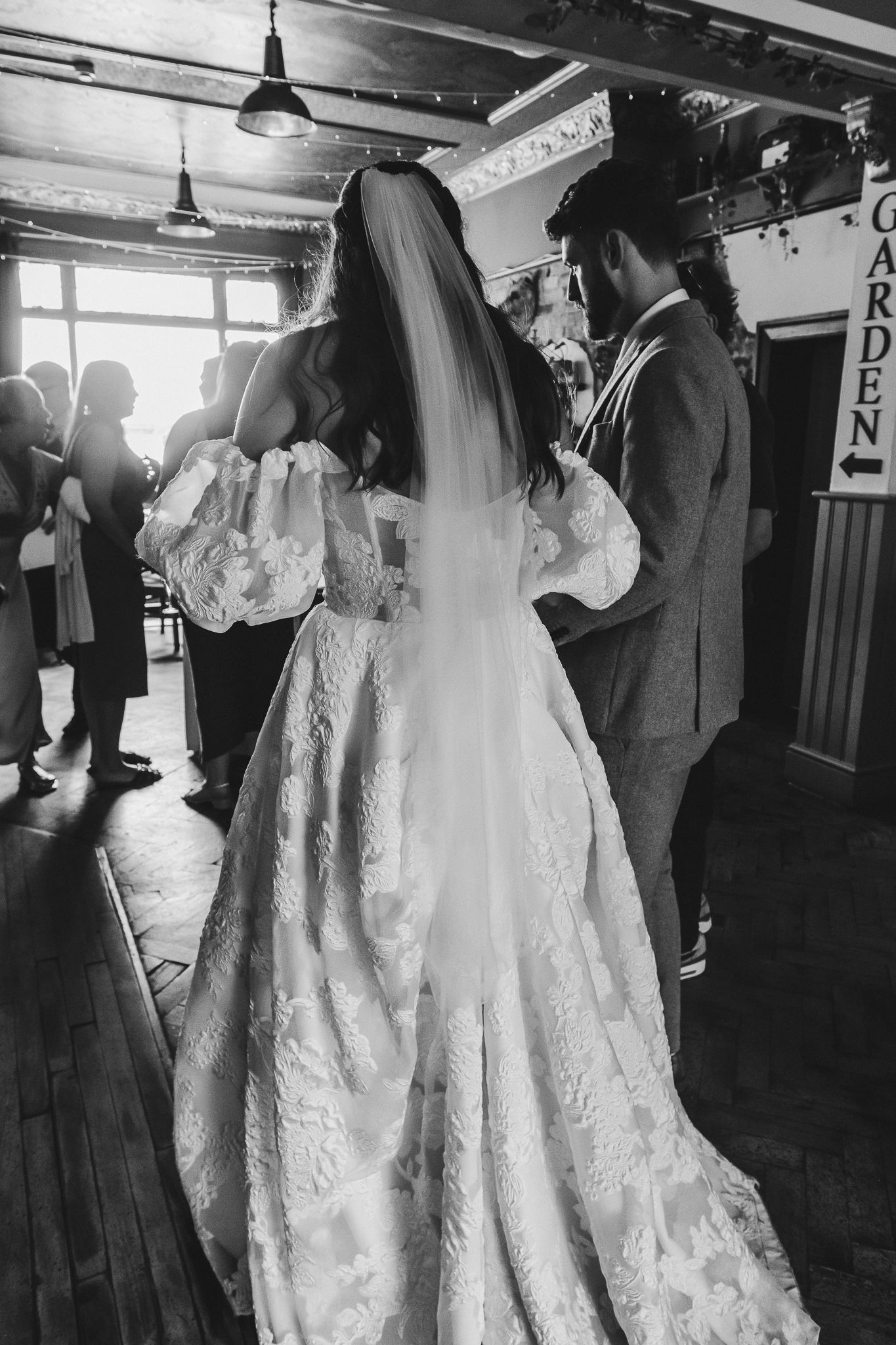 Black and white wedding photos show a bride in a lace gown with a flowing veil during an intimate indoor celebration.