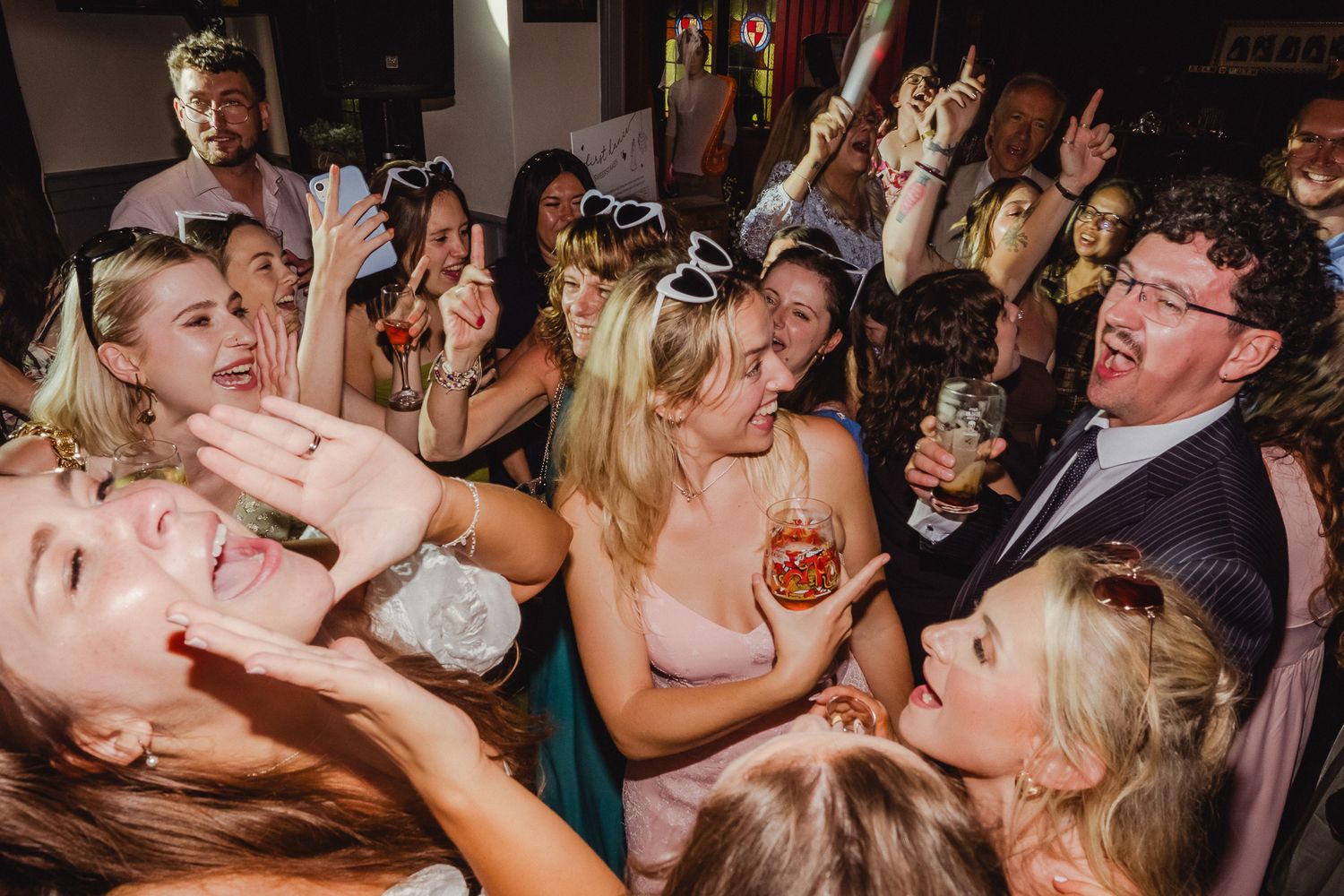 A lively crowd of party guests dancing and celebrating enthusiastically on a crowded dance floor at a nighttime event.