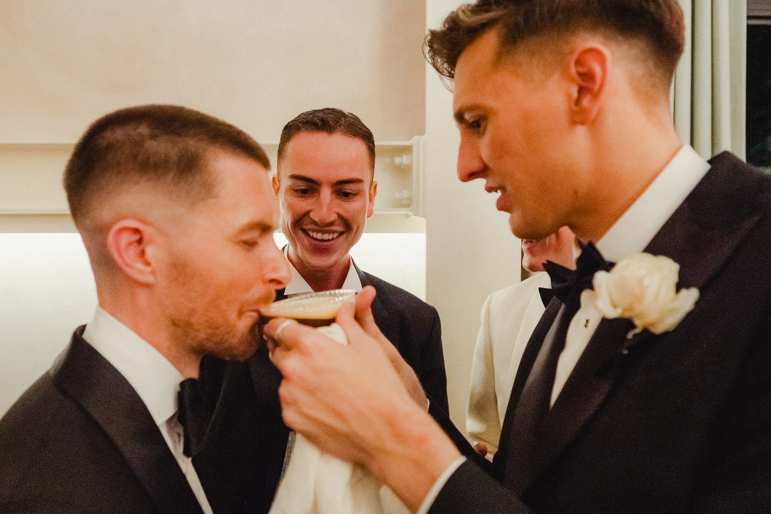 Three people in black suits and bowties share a lighthearted moment together at a formal event.