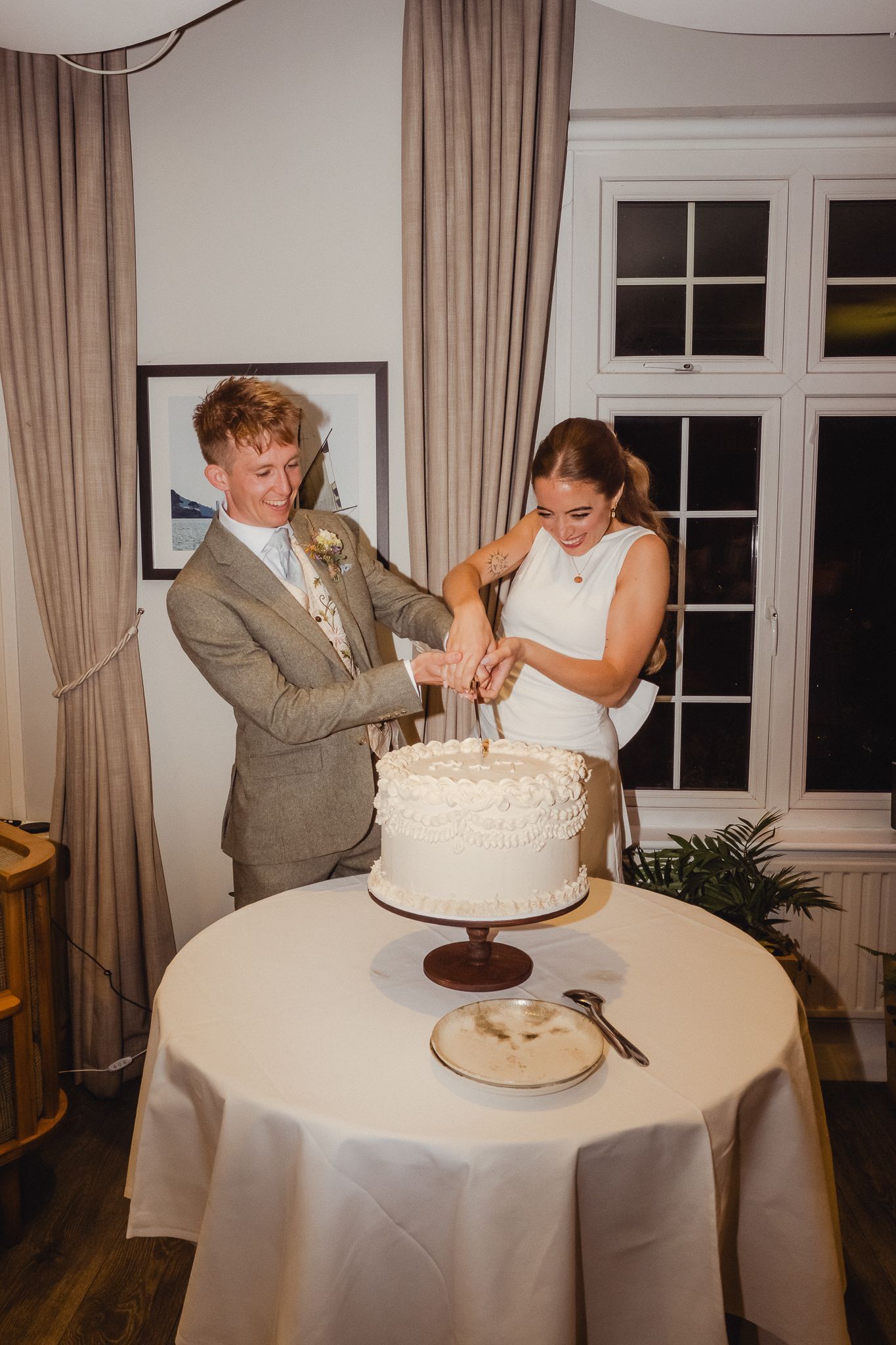 A couple feeds each other wedding cake in a series of candid reception photos at a white-tableclothed venue.
