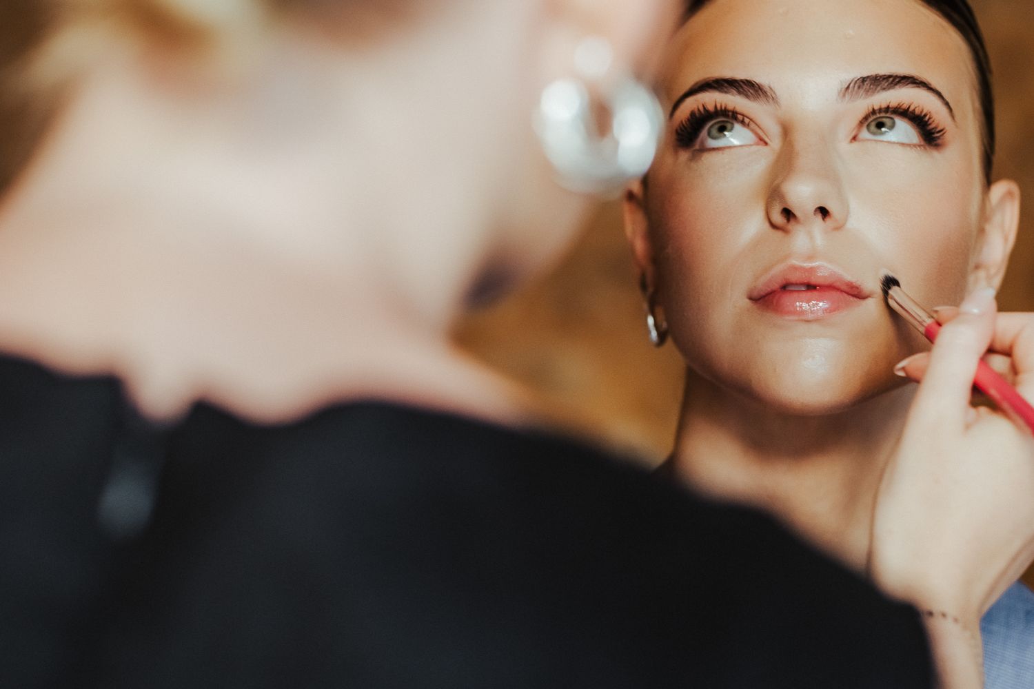 Makeup artist applies cosmetics to model's face during professional beauty session in warm lighting.