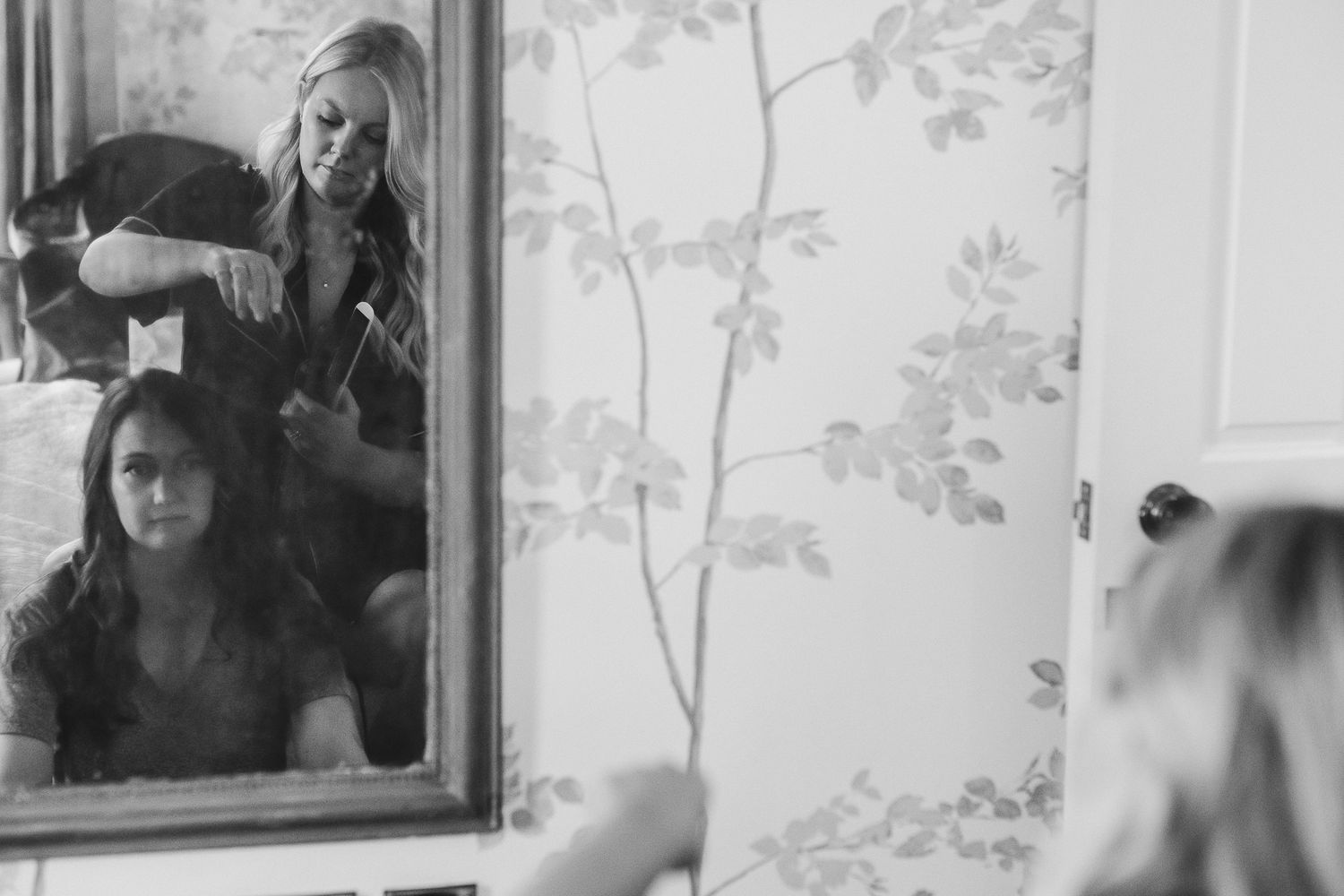 A black and white photograph shows a person looking into a mirror while wearing a dark cap.