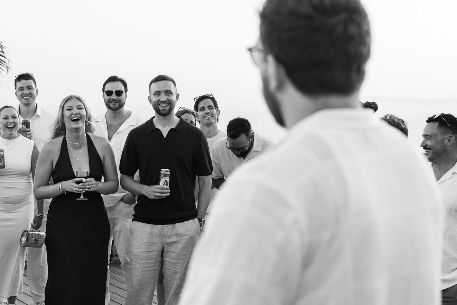 Group of smiling guests enjoying drinks at an outdoor beach party celebration in black and white photo.