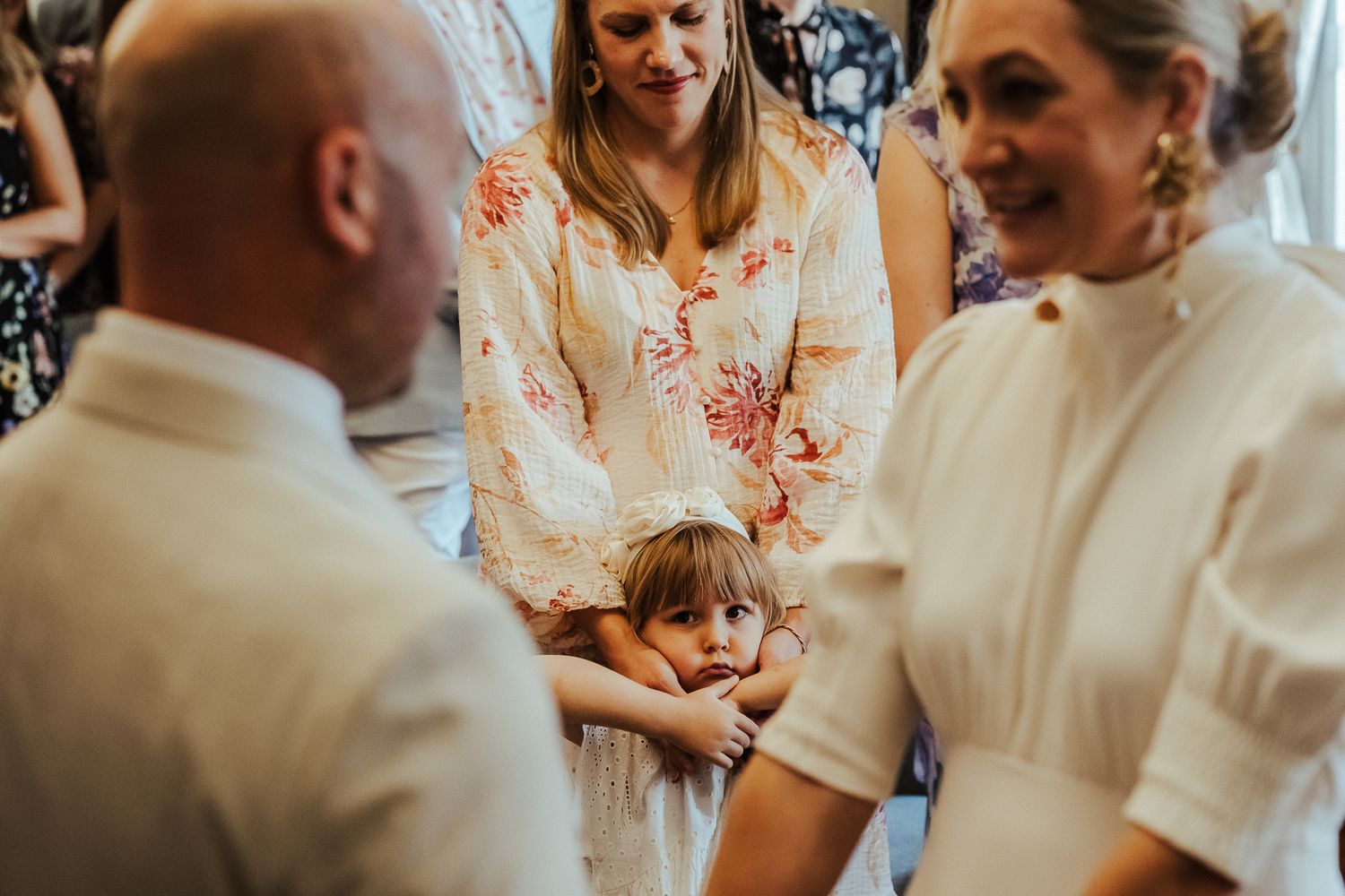 A child holds hands with adults wearing white and floral attire during what appears to be a special ceremony.