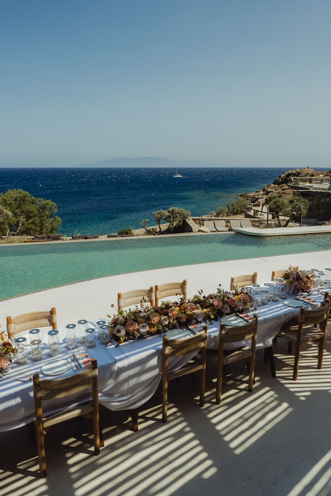 Long banquet tables with wooden chairs overlooking a stunning turquoise ocean view at a coastal wedding venue.