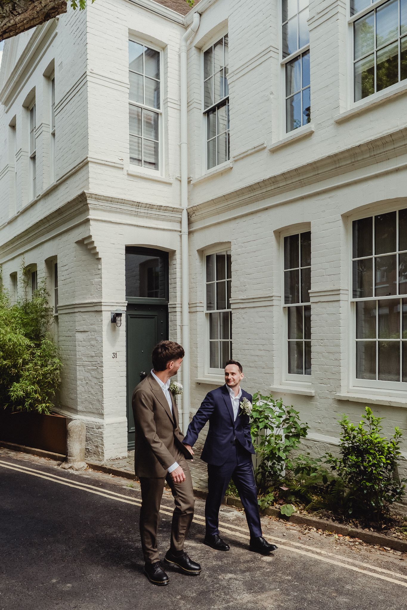 Two people in business attire having a conversation outside a white brick building with tall windows.