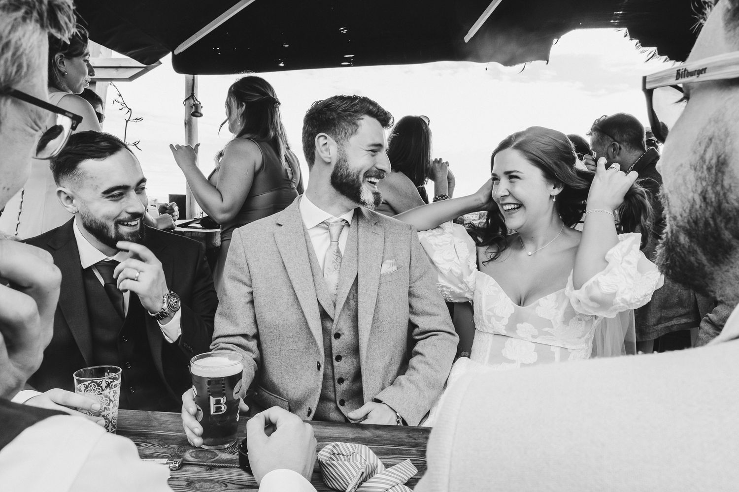 Black and white candid photo of wedding guests sharing a joyful moment together at an outdoor reception.