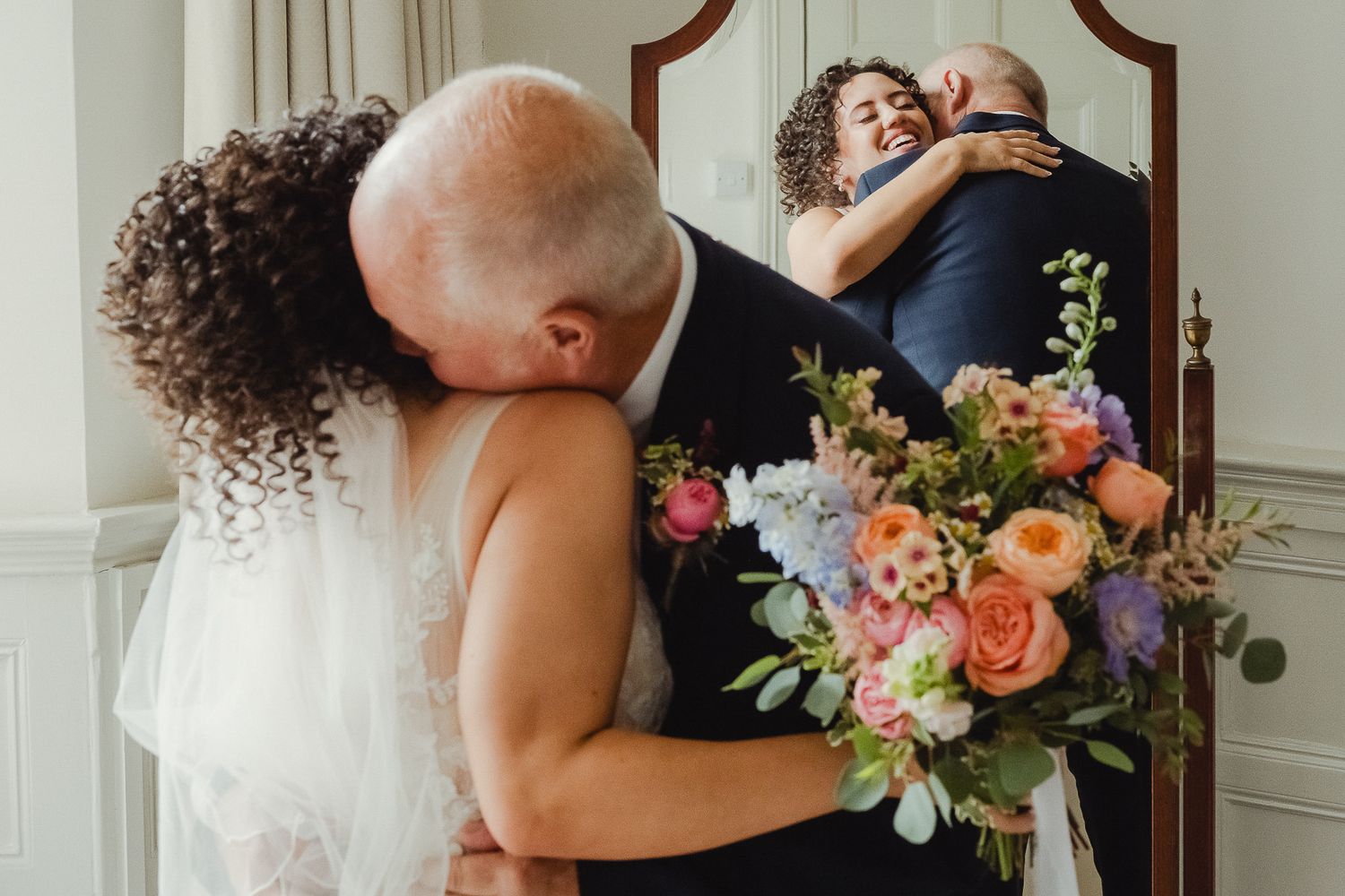 A romantic wedding couple shares an intimate moment in front of a mirror with a beautiful floral bouquet.