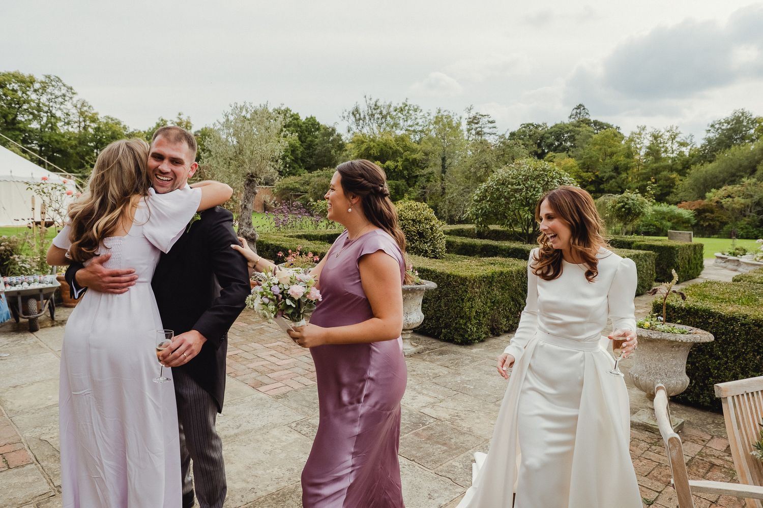Joyful wedding celebration on an outdoor patio surrounded by lush garden hedges and greenery.
