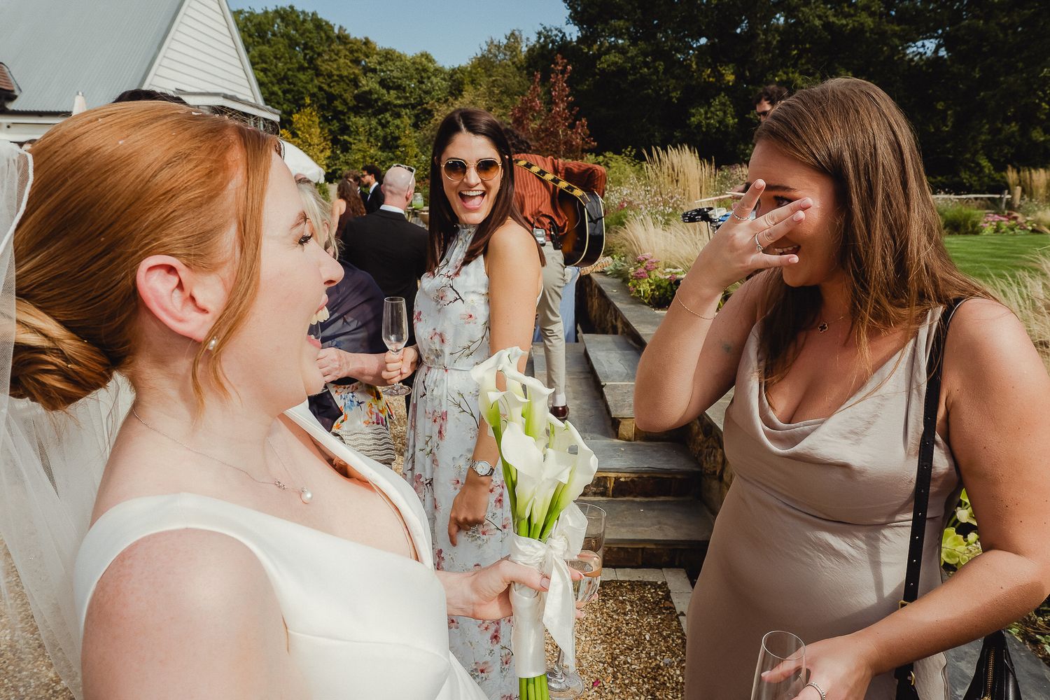 A group celebrates at an outdoor wedding reception, laughing and raising glasses in a toast.