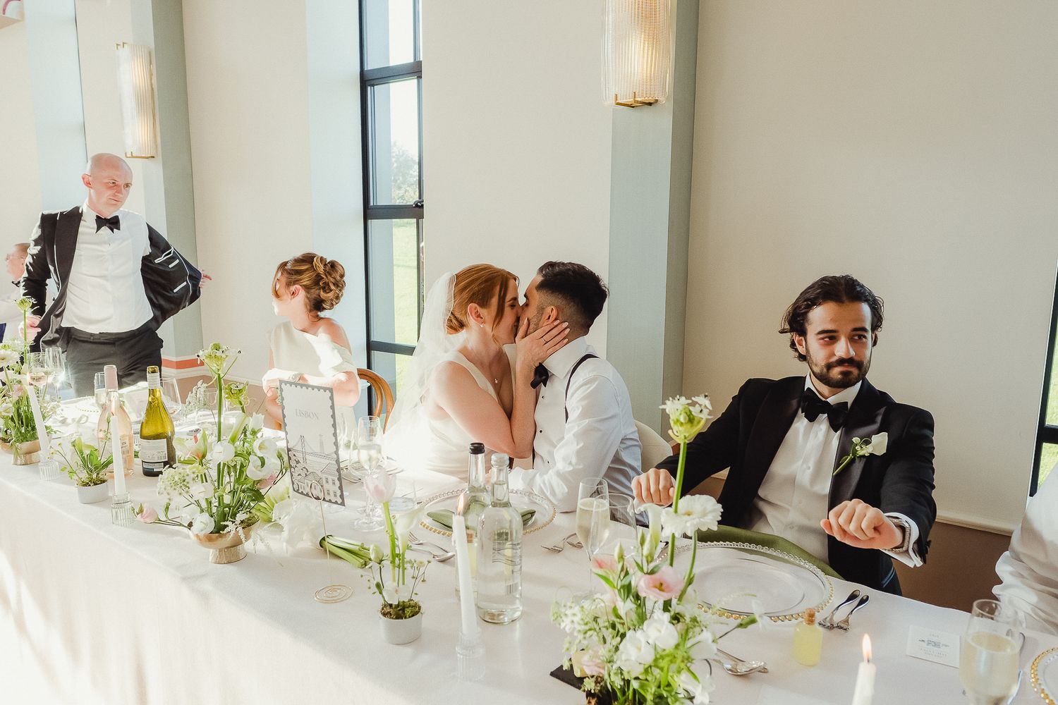 Wedding guests seated at elegant dining tables decorated with white floral centerpieces and glassware.