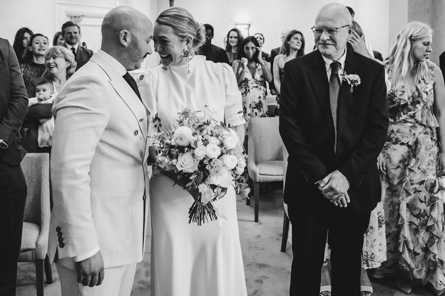 A wedding party arranged in a line poses together with bouquets and formal attire during an outdoor celebration.