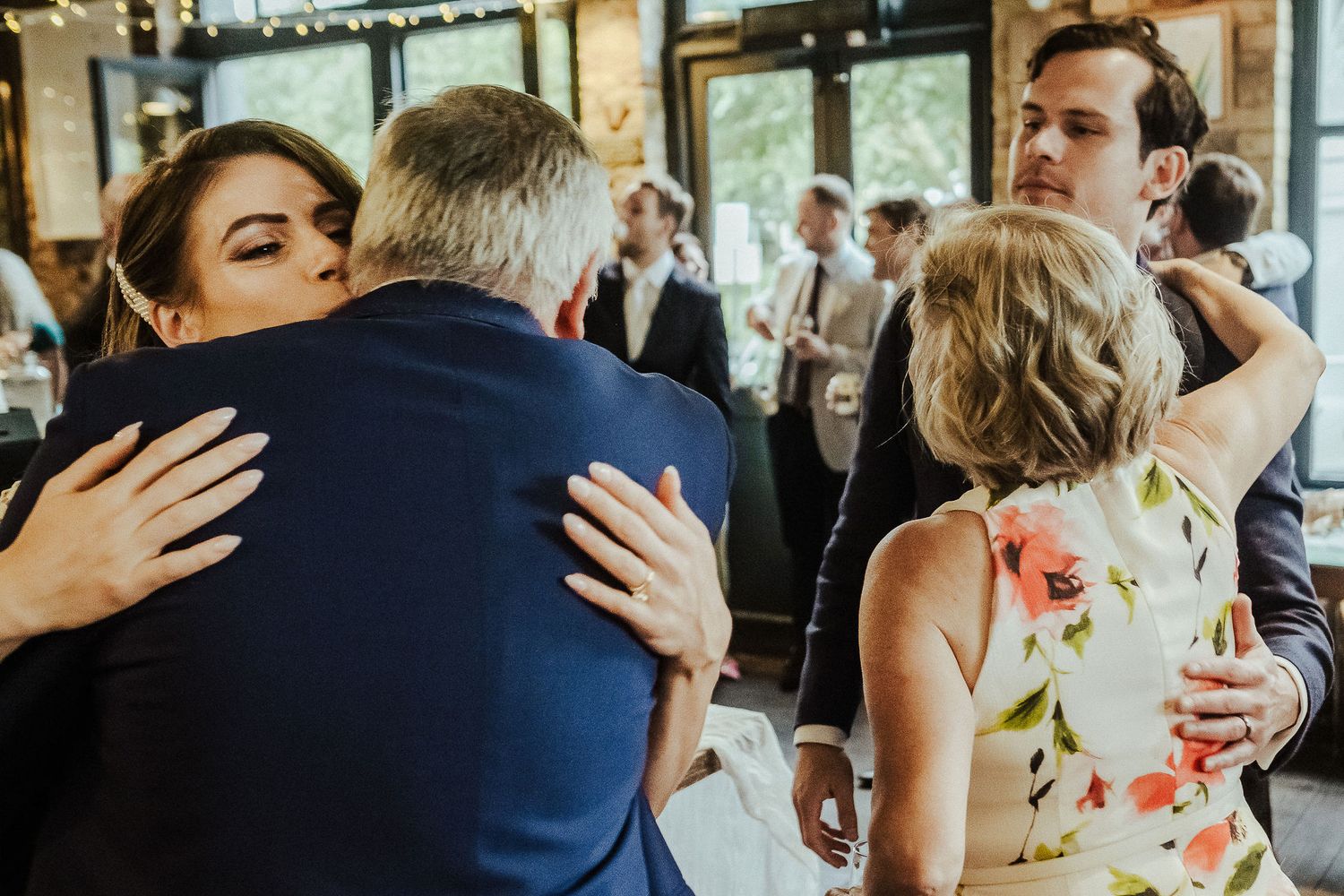 Wedding guests embrace and share emotional moments during a reception celebration in an indoor venue.