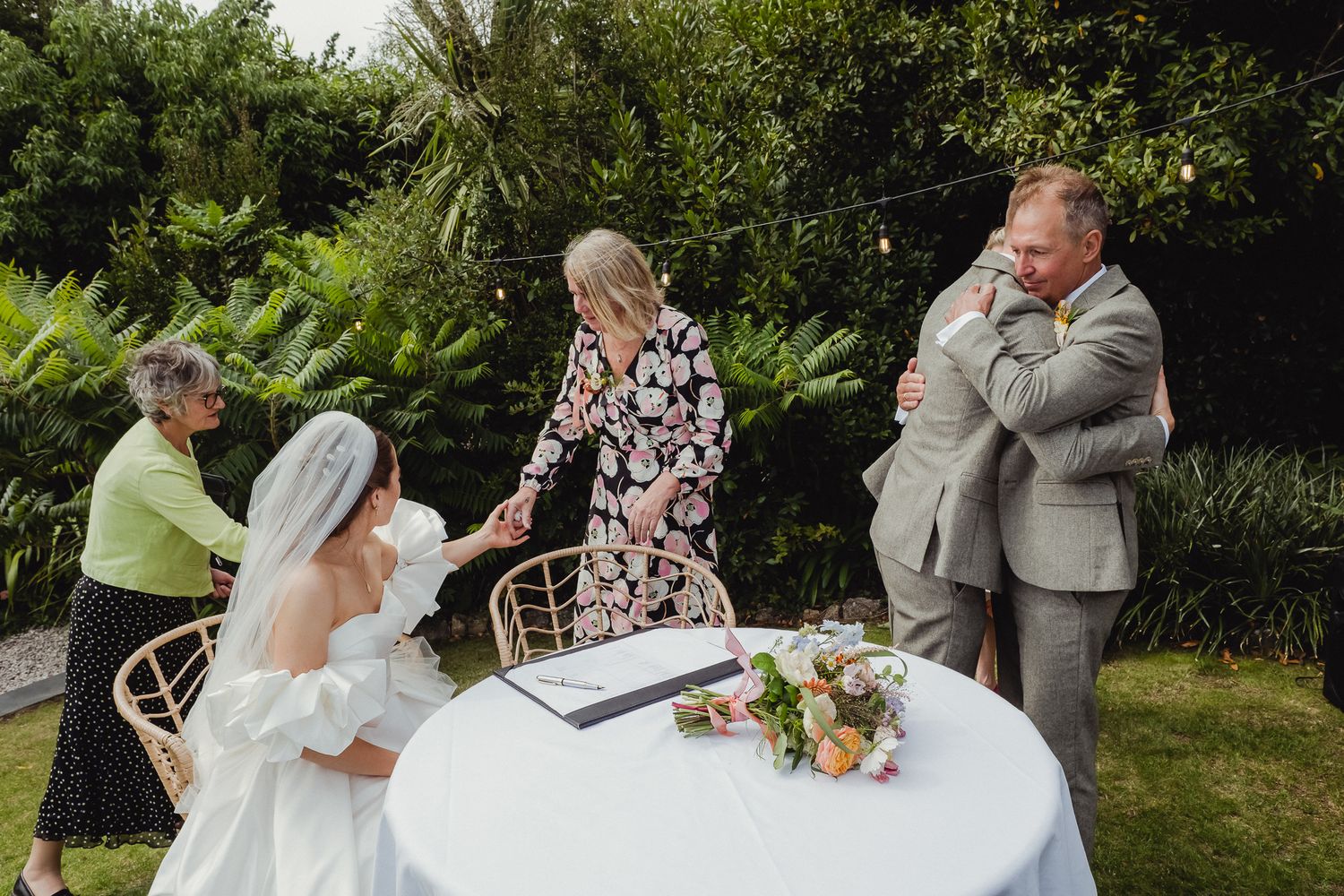 A bride and groom share a romantic kiss during an outdoor garden wedding ceremony surrounded by guests.