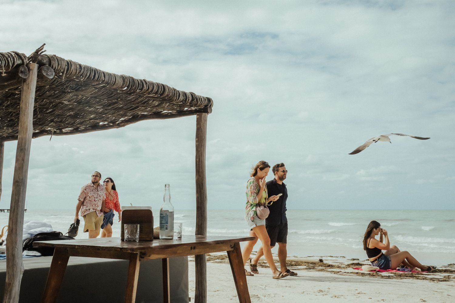 Beachgoers relax under thatched umbrellas on a cloudy day at a tropical beach resort.