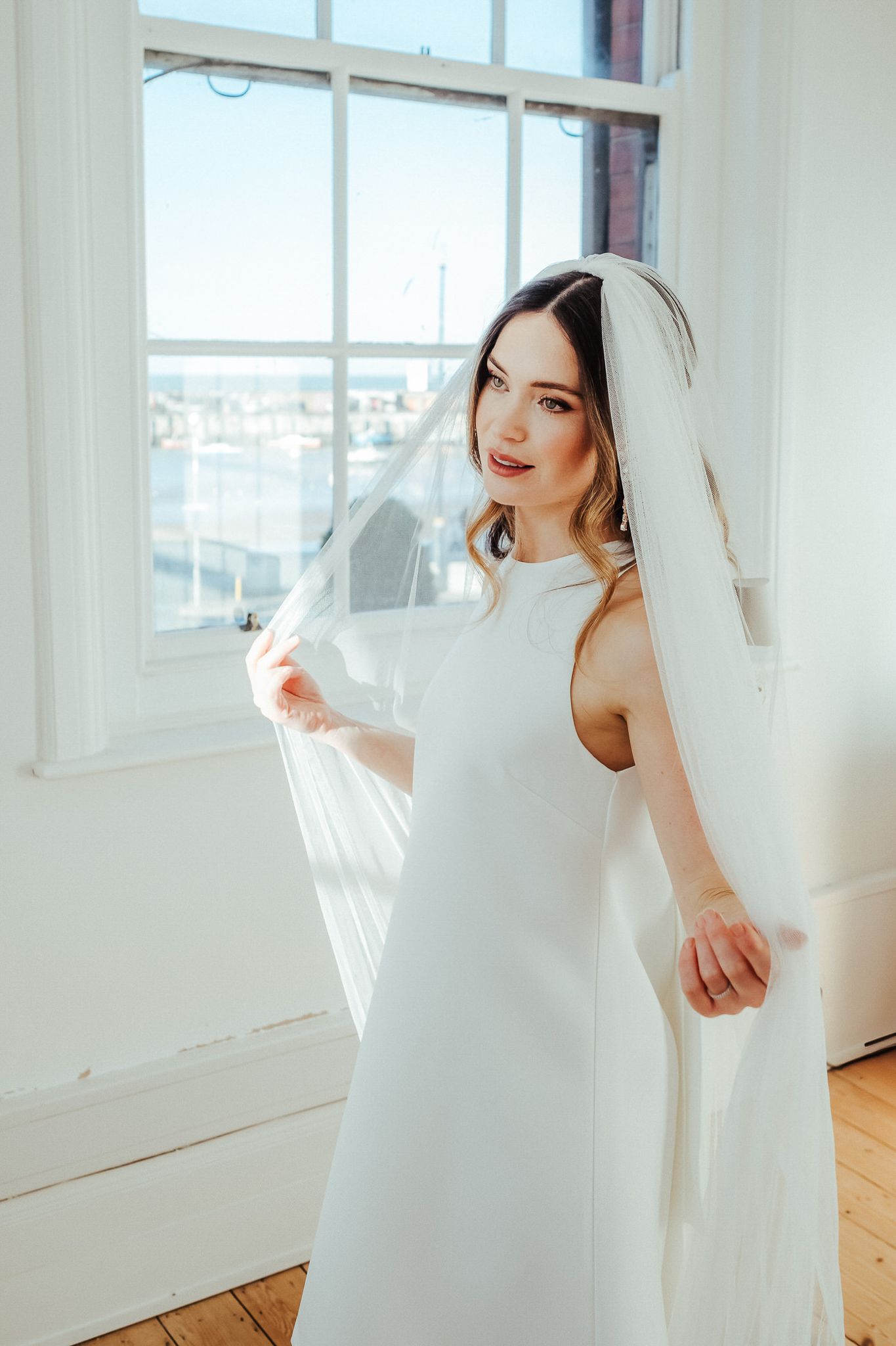 Ethereal bridal portrait in a sunlit white studio with flowing fabric and soft natural lighting.