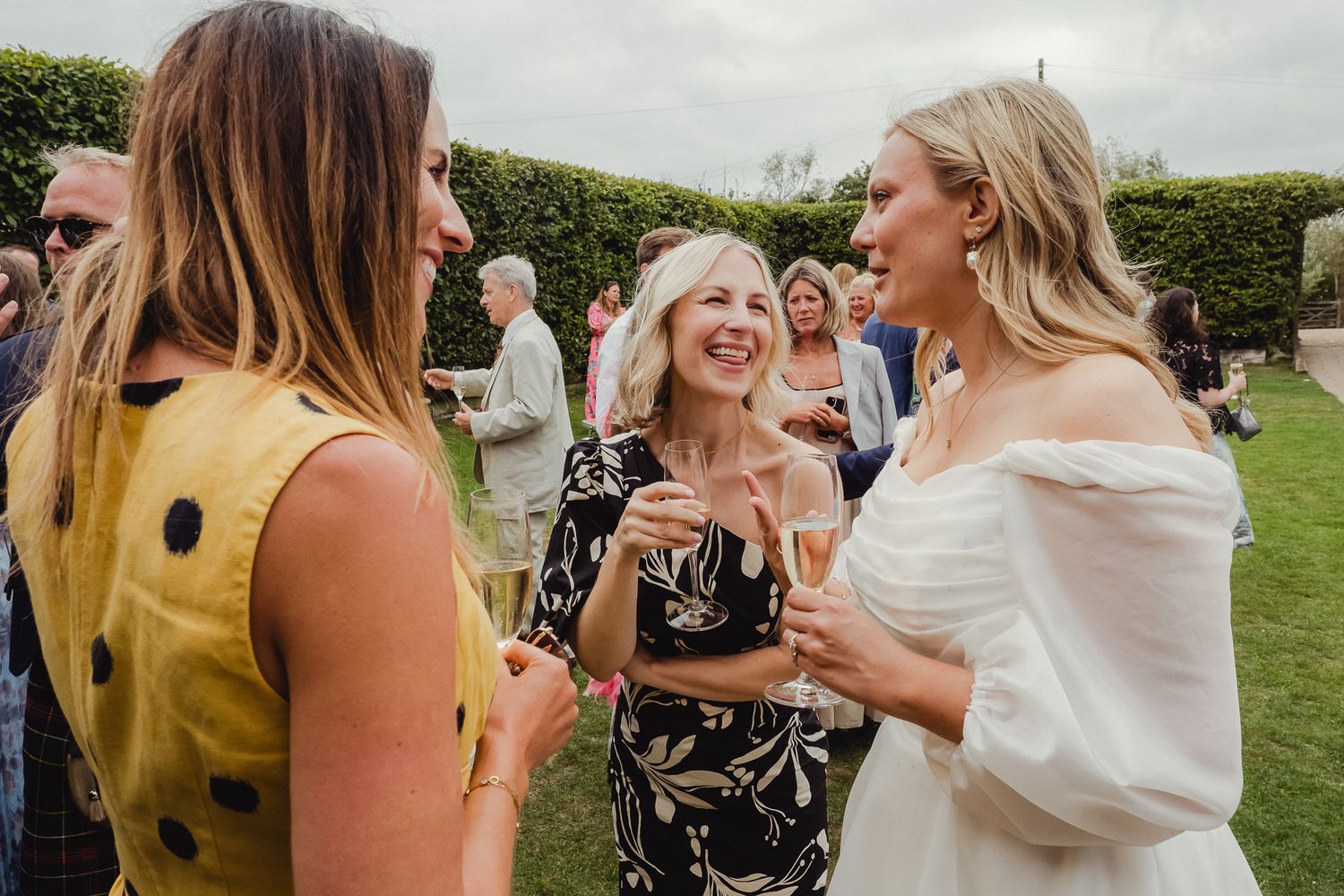 A group of wedding guests mingle and chat during an outdoor reception on a grassy lawn.
