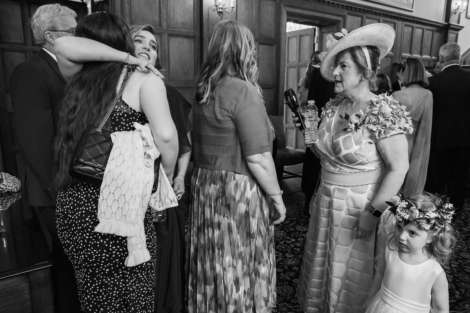 Black and white wedding photo of guests socializing, including a flower girl in a floral crown.