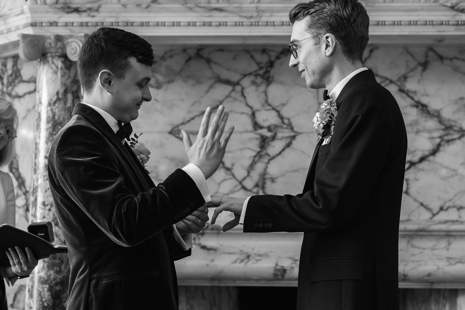 Two grooms exchange rings at wedding ceremony in elegant marble venue, black and white photo.