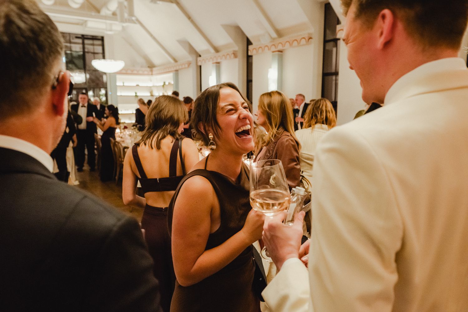 A joyful moment of dancing and laughter at an elegant indoor wedding reception under white tent lighting.