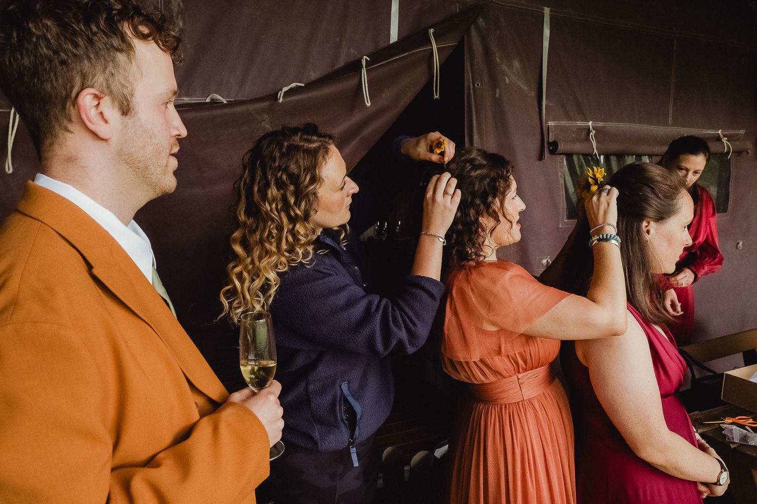 Wedding party members stand in line wearing orange, navy and burgundy attire at an indoor venue.