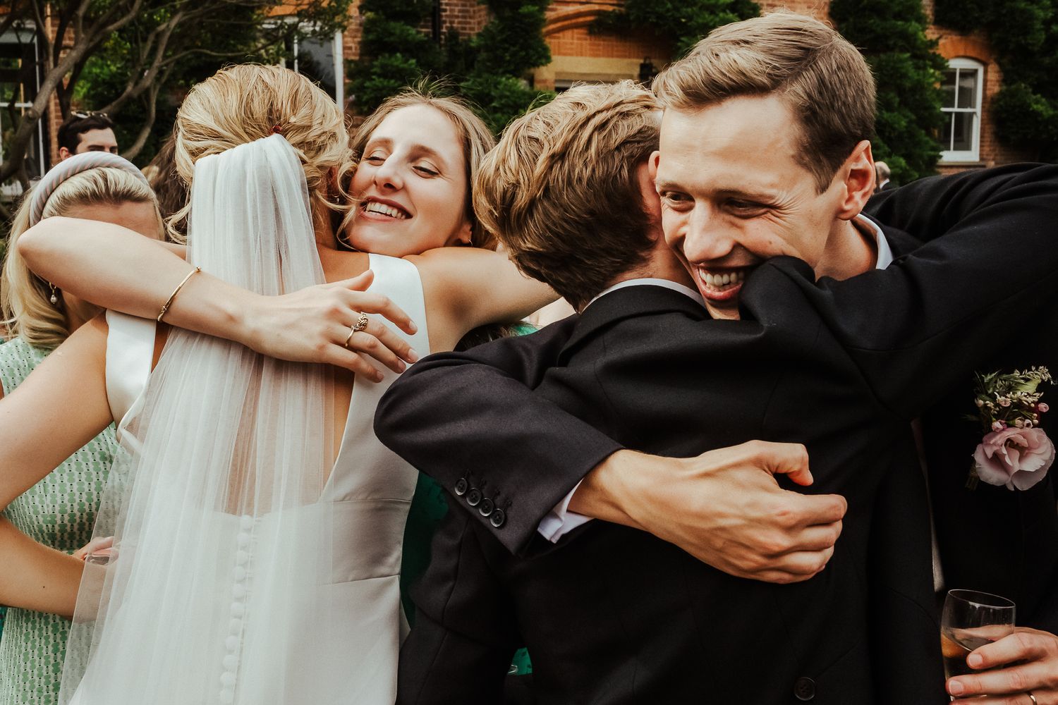 A group of wedding guests share emotional hugs during outdoor celebration.