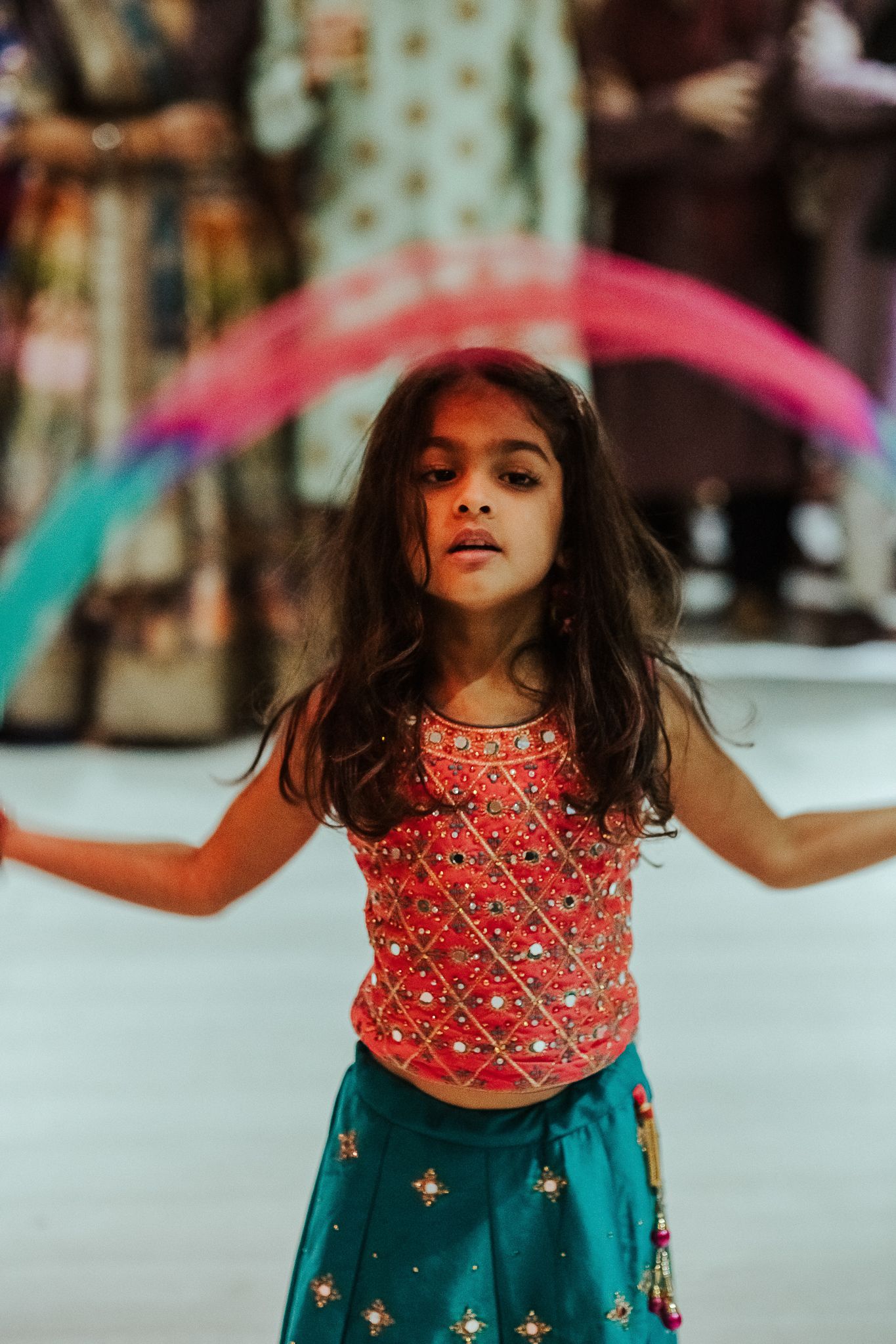 Young dancer in a red sequined top and teal skirt performing at a cultural celebration.