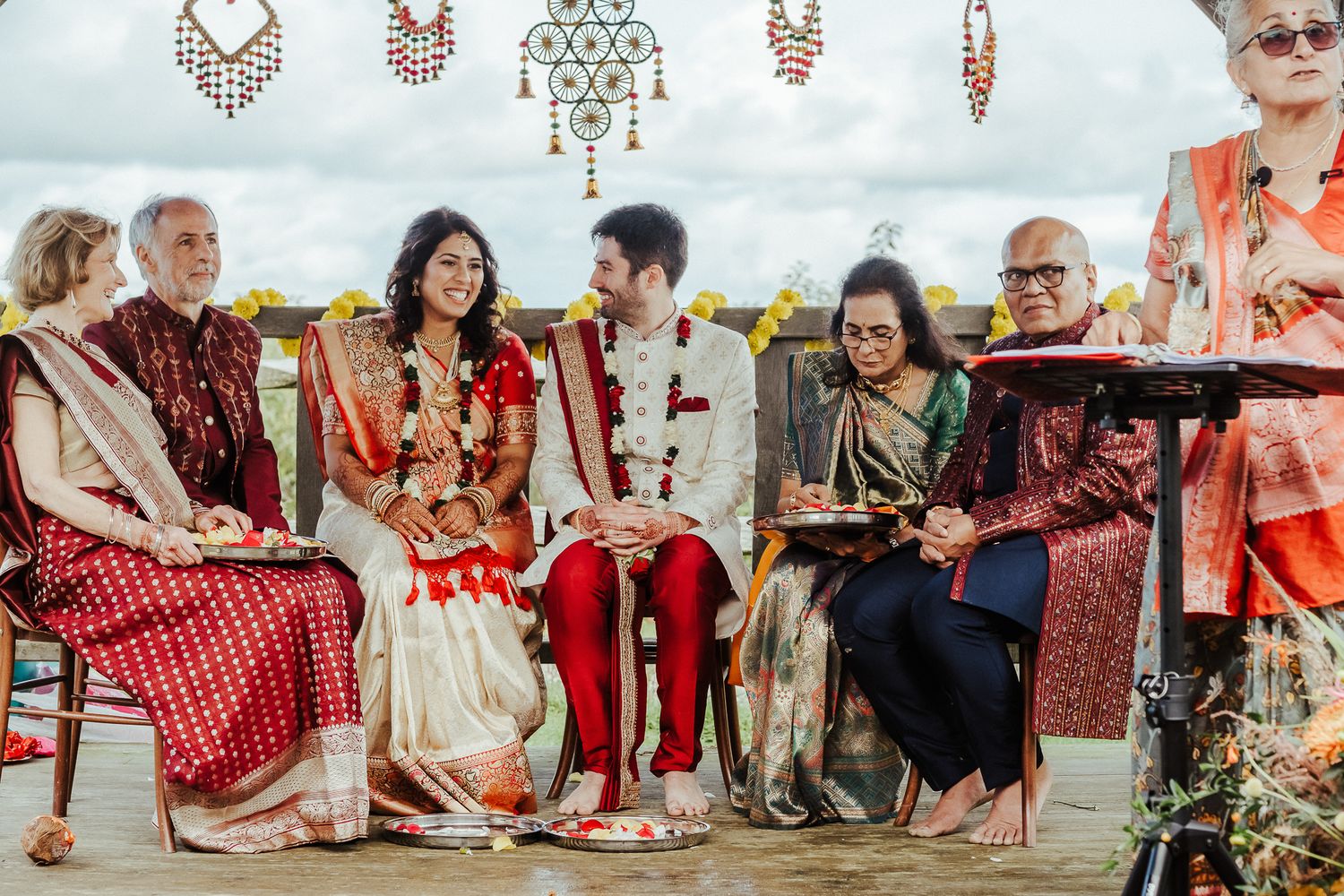 Family members in traditional Indian wedding attire seated together during an outdoor ceremony.