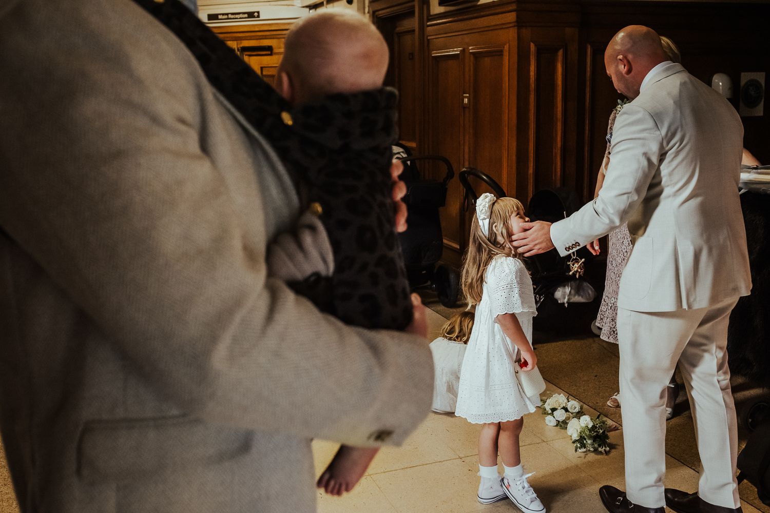 Man in light colored suit holds hands with young girl in white dress during what appears to be a wedding celebration.