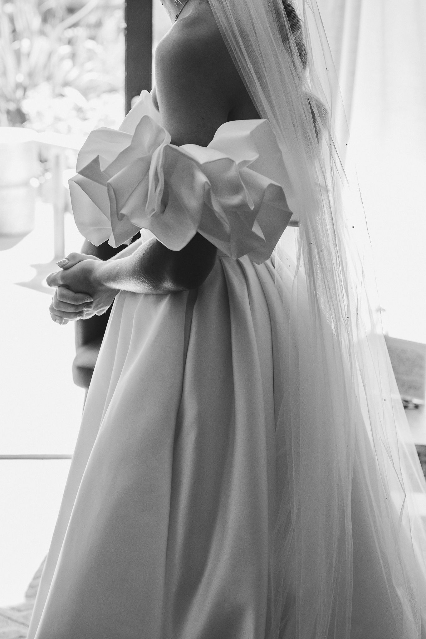 Elegant white wedding dress with flowing tulle veil captured in a soft black and white photograph.