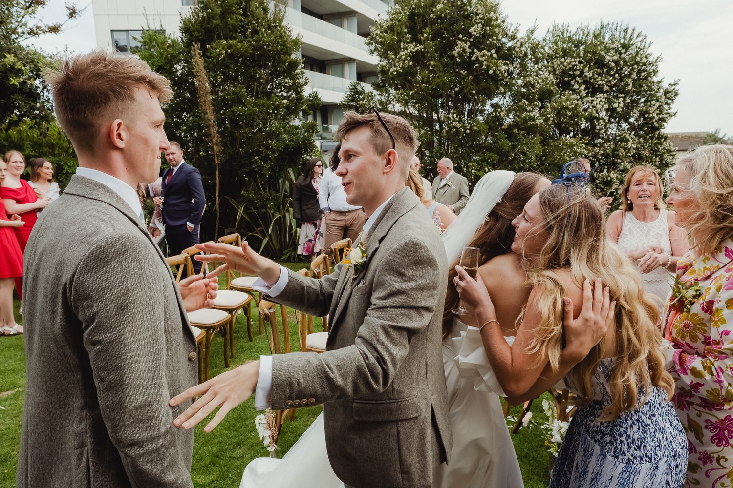 Wedding guests celebrate outdoors during a summer garden reception with people clapping and laughing.