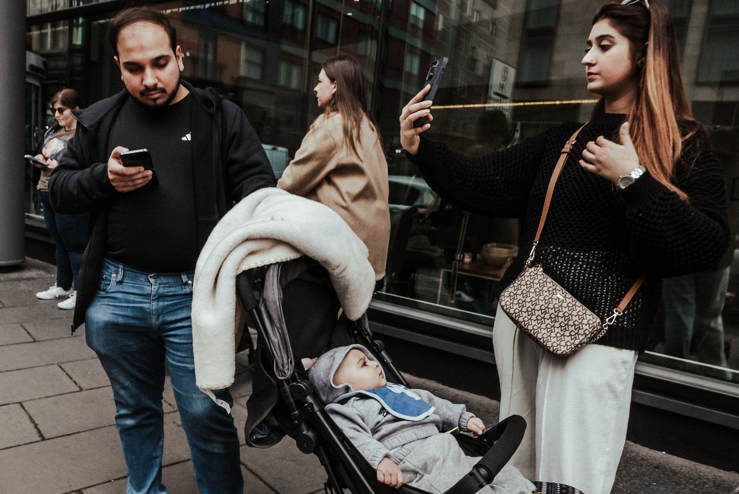 People on a city street looking at mobile phones while standing near storefront windows.
